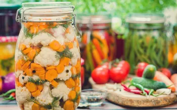 A table full of vegetables on a wooden cutting board and sealed in jars for pickling.