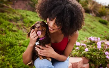 Smiling young woman sitting with her cute little dachshund outside