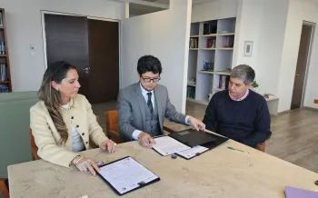 Two people signing an agreement, sitting at a table.
