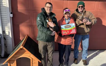 a group of people standing next to a doghouse, holding dogs and treats