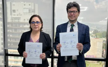 Two people standing, each holding a signed document.