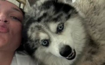 person is taking a close-up selfie on a couch with a fluffy dog