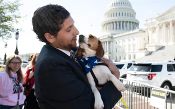 A person holding a small dog outside the United States Capitol building.