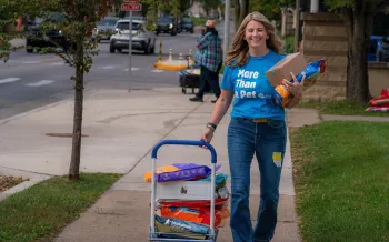  Smiling woman walking, pulling a small cart loaded with large bags of pet food.