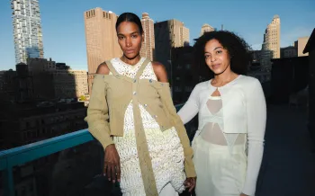 Two people pose together on a rooftop at sunset with a city skyline of tall buildings behind them.
